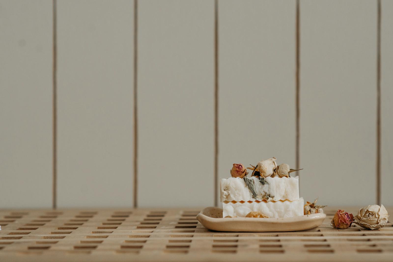 Studio still life of a vanilla amber body butter jar, dried botanicals, and a brass spoon on warm linen.